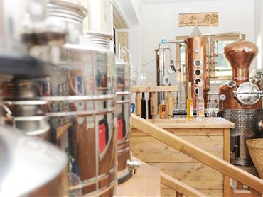 Eine Brennerei mit modernen Geräten aus Edelstahl und Kupfer. Holzregale und eine warme Atmosphäre prägen den Raum.
