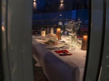 Ein elegant gedeckter Tisch mit Kerzen und gedeckten Gläsern. Im Hintergrund sieht man eine Flasche Wein und eine ansprechende Dekoration.