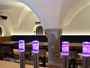 Ein modernes Restaurant mit stilvollen Holztischen und sanfter Beleuchtung. Die Wände sind aus Stein und die Decke hat schöne Gewölbe.