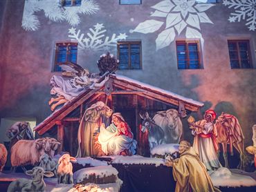 Eine festliche Krippe mit Maria, Josef und dem Jesuskind in einer Stall-Szene. Umgeben von Tieren und einer winterlichen Dekoration.