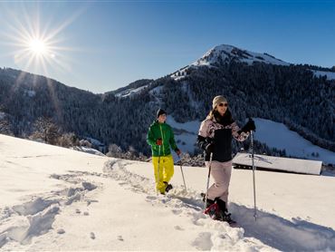 Zwei Personen wandern im Schnee in den Bergen. Die Sonne scheint klar und der Himmel ist blau.