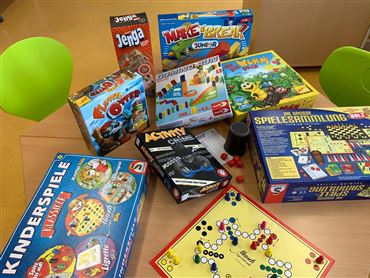 Eine Auswahl von Brettspielen liegt auf einem Tisch. Die Spiele sind bunt und reichen von klassischen bis zu modernen Kinderspielen.